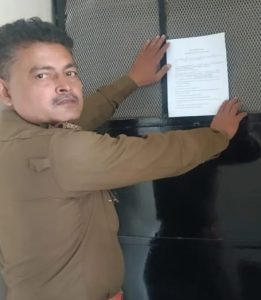 फाइल फोटो -नेहा सिंह राठौर के घर नोटिस चस्पा करता पुलिस कर्मी 